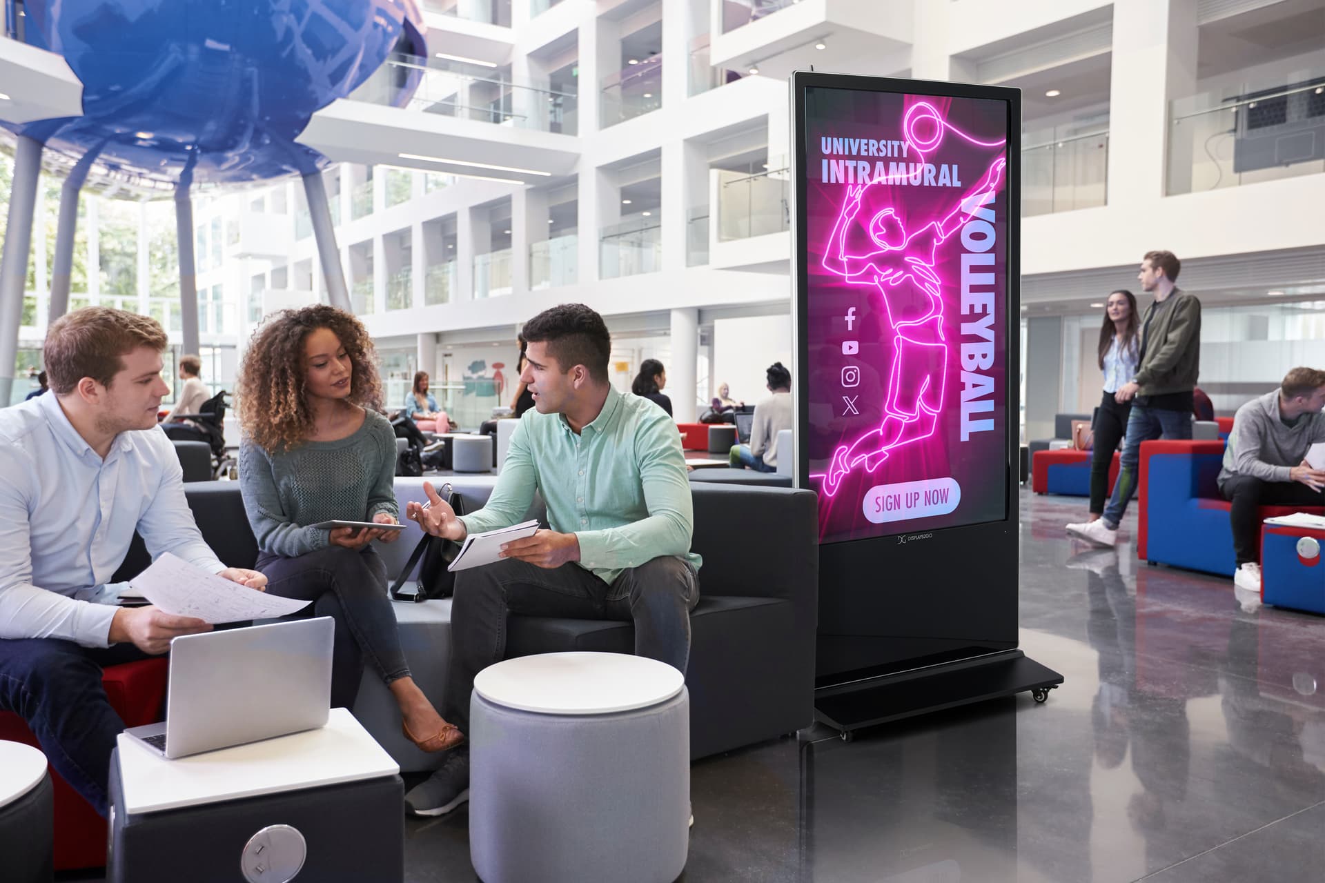 Advertising multimedia kiosk being used at a university common area displaying a volleyball intramural graphic
