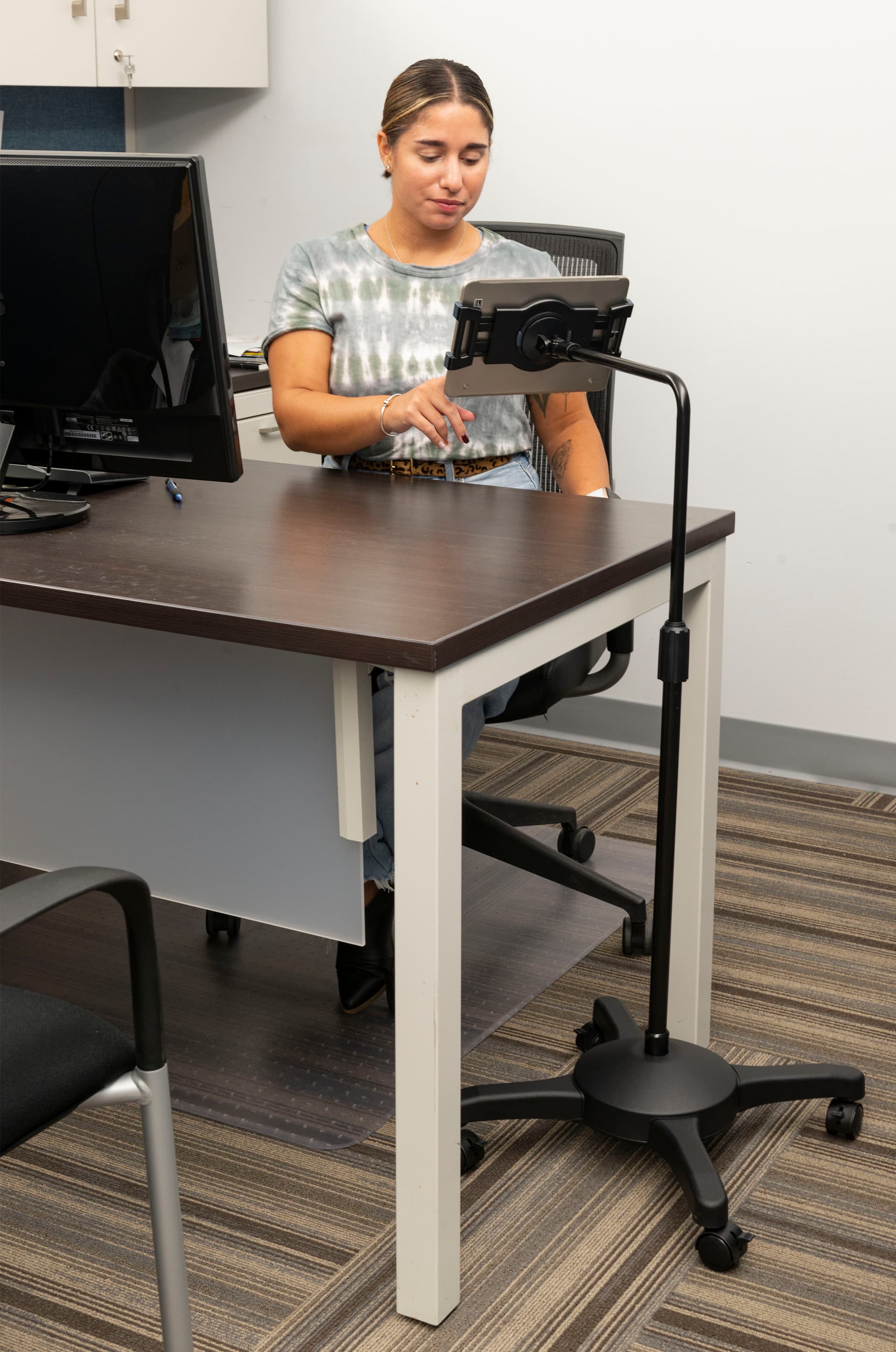 L-arm adjustable tablet holder with wheels shown in an office setting