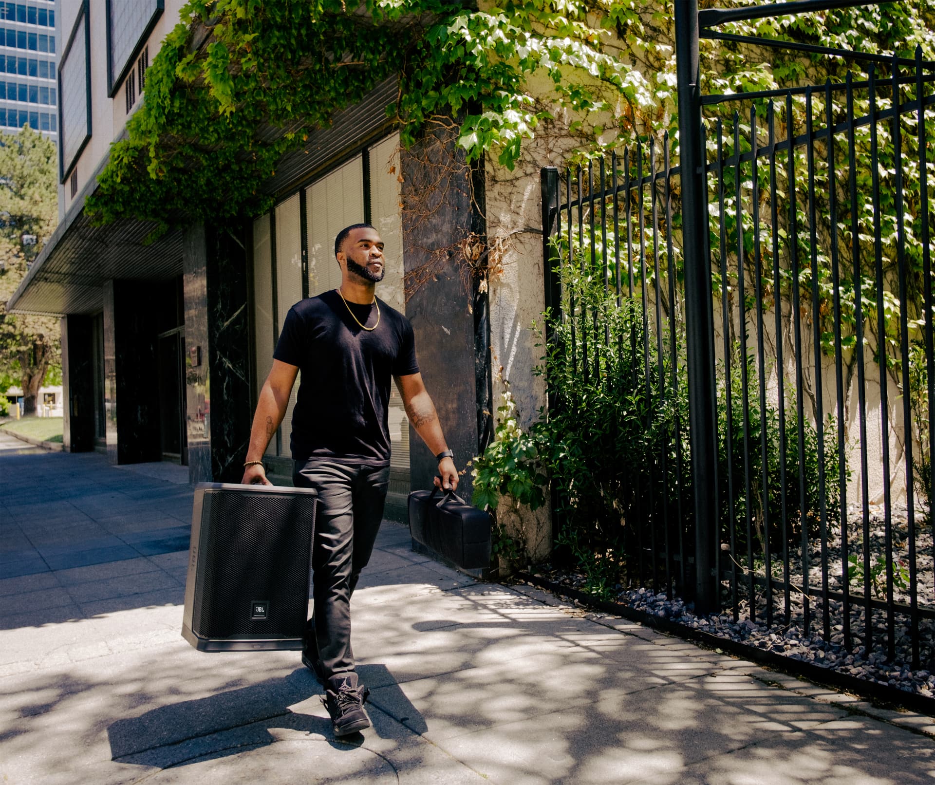 JBL column speakers being carried by one individual on a side walk in a metropolitan area